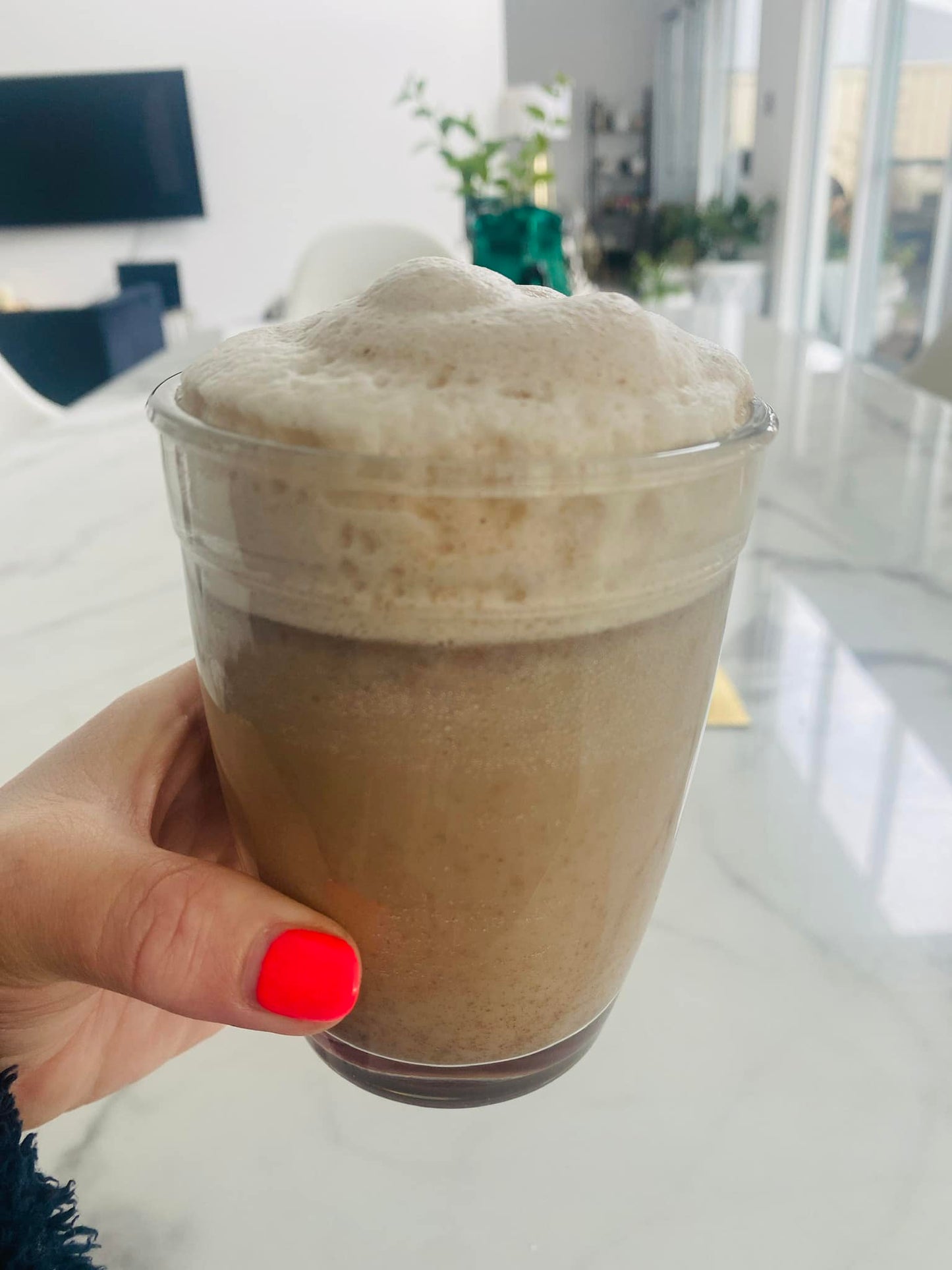 Hand holding a cup of foamy Chai Collagen Latte