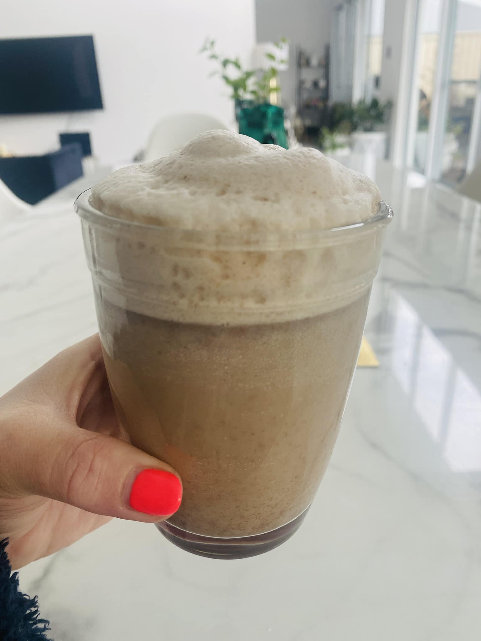Hand holding a cup of foamy Chai Collagen Latte