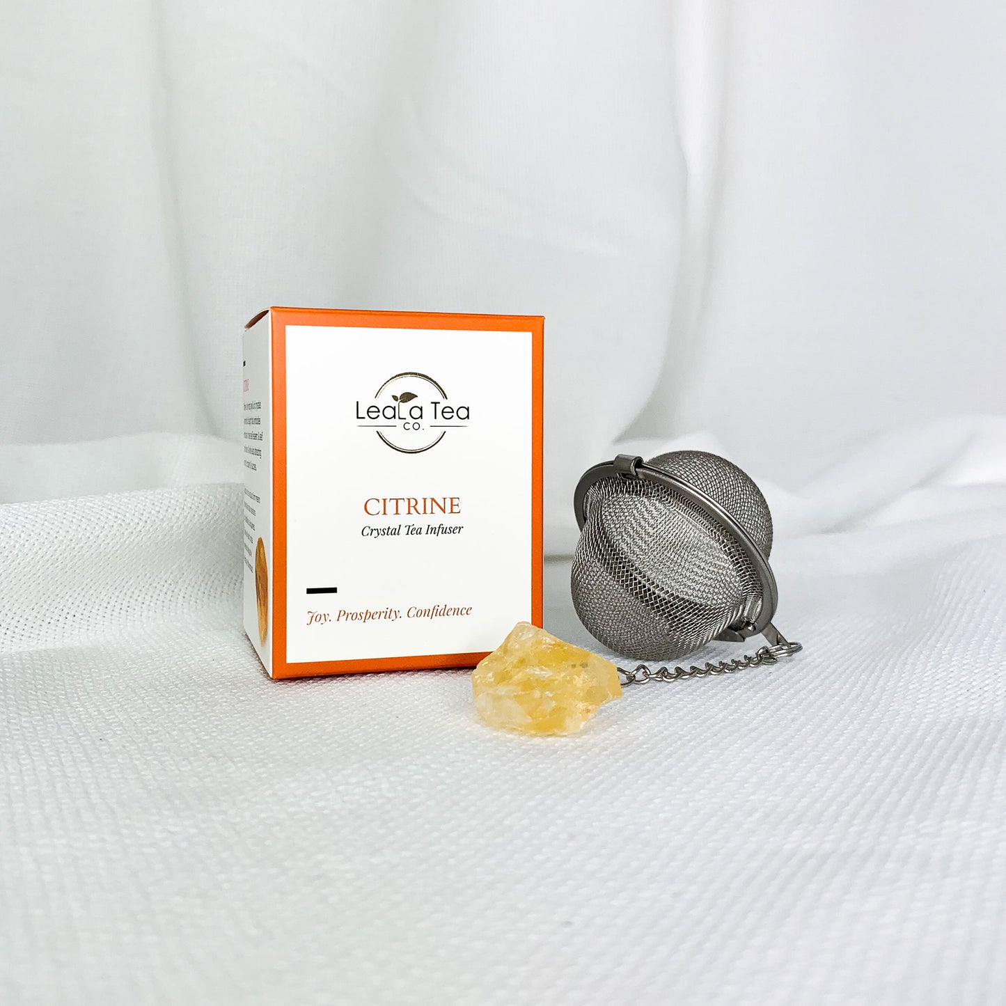 Athella Citrine Crystal Tea infuser, Joy, Prosperity, Confidence box packaging next to round Citrine Crystal Tea Infuser with Citrine at end of chain.