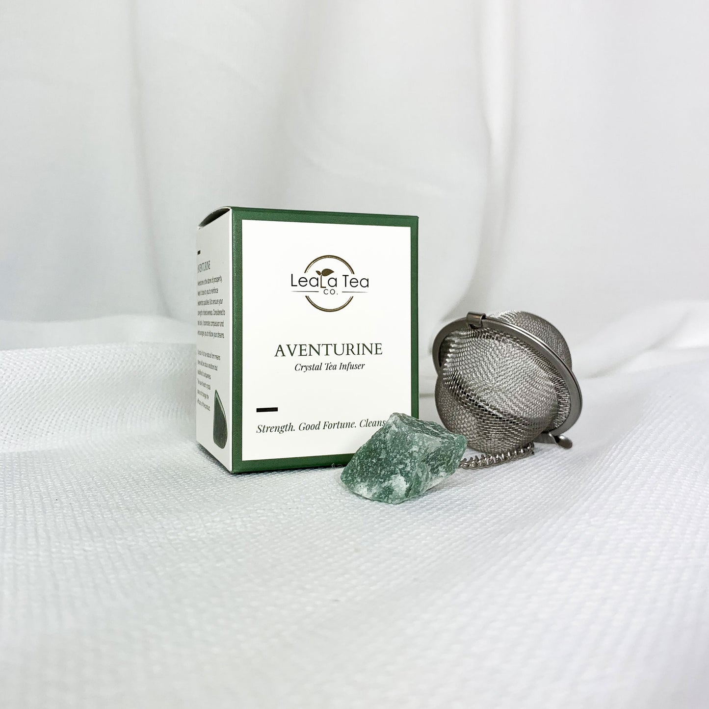 Athella Aventurine Crystal Tea Infuser, Strength, Good Fortune, Cleanse box packaging next to round tea strainer with aventurine on end of chain. 